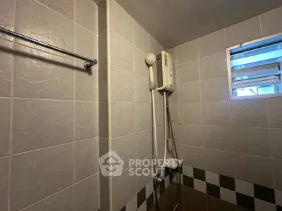 Compact bathroom with tiled walls and electric shower heater, ideal for small apartments.