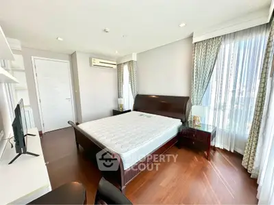 Spacious bedroom with elegant wooden flooring and large windows offering natural light.