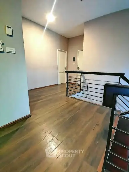 Spacious hallway with wooden flooring and modern railing in a residential building.