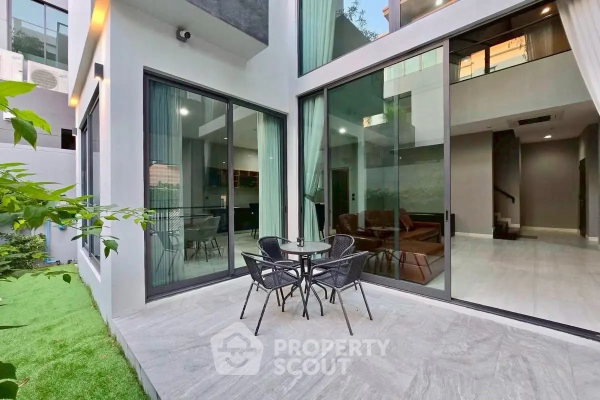 Modern home exterior with large glass doors opening to a stylish patio and lush green lawn.