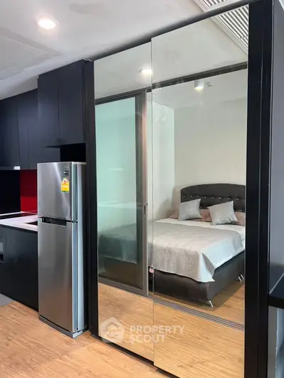 Modern studio apartment with sleek kitchen and cozy bedroom separated by glass partition.