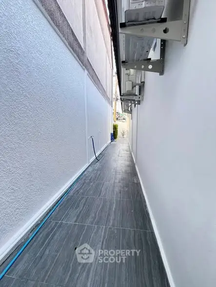Narrow outdoor corridor with tiled flooring and white walls, ideal for utility or service access.