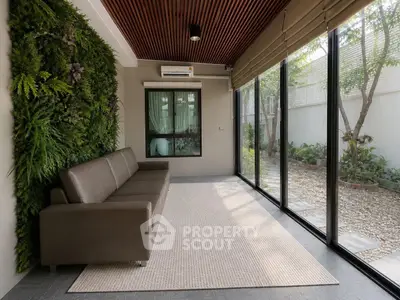 Modern living room with glass walls and garden view, featuring a sleek sofa and vertical garden.