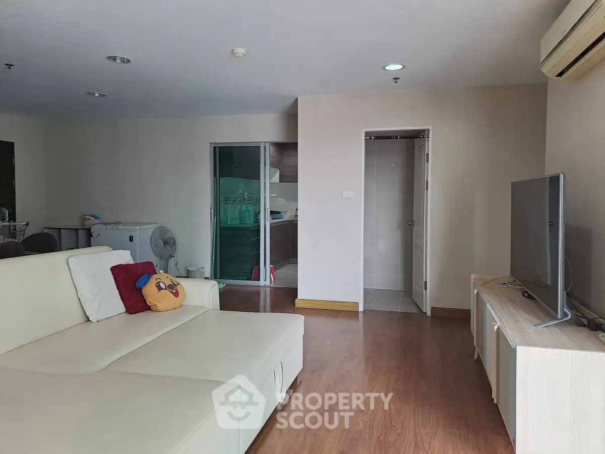 Spacious living room with modern decor and natural light, featuring a comfortable sofa and large TV.
