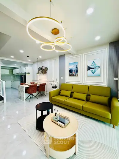 Modern living room with stylish green sofa, elegant lighting, and open kitchen layout in a contemporary home.