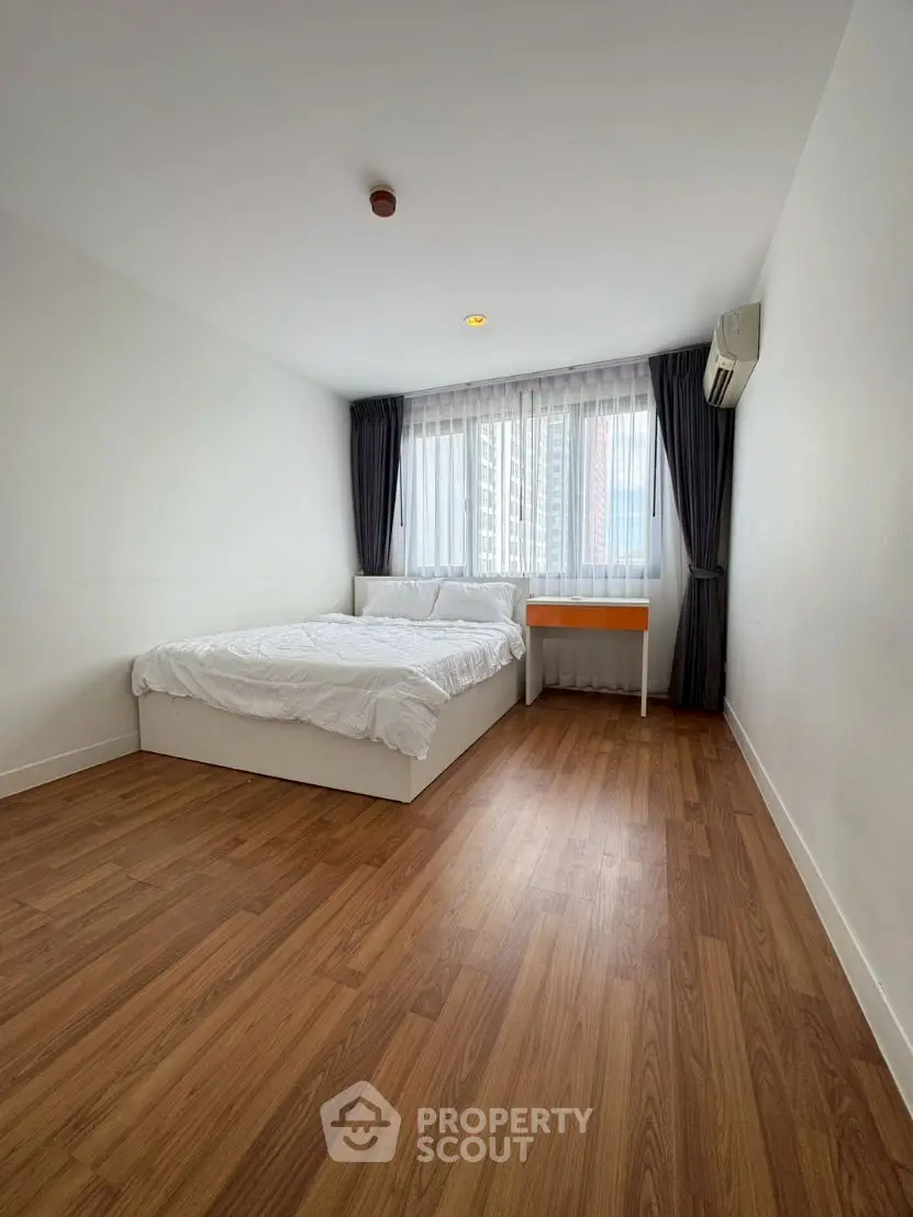 Spacious bedroom with wooden flooring and large window in modern apartment