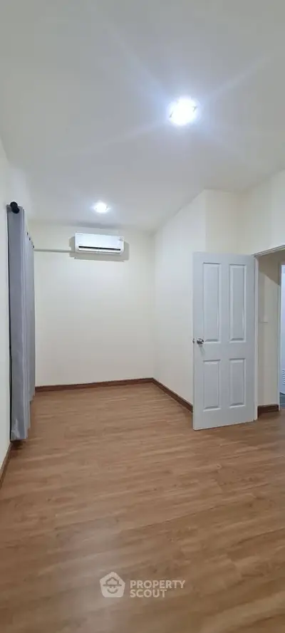 Spacious empty room with wooden flooring and air conditioning, perfect for customization.