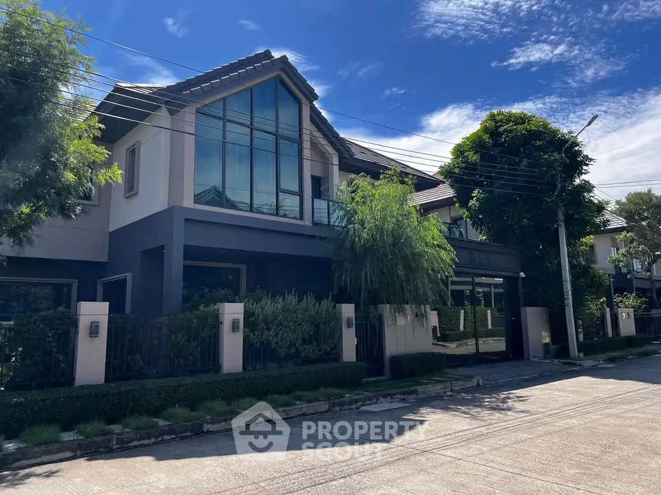 Modern two-story house with large windows and lush greenery in a suburban neighborhood.