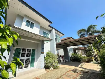 Modern two-story house with carport and lush greenery under clear blue sky.