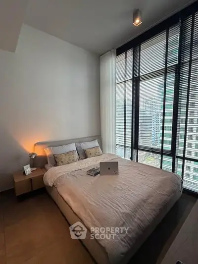 Modern bedroom with large windows offering city views, featuring a cozy bed and stylish decor.