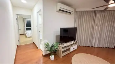 Modern living room with wooden flooring, TV unit, and air conditioning, leading to a cozy bedroom.