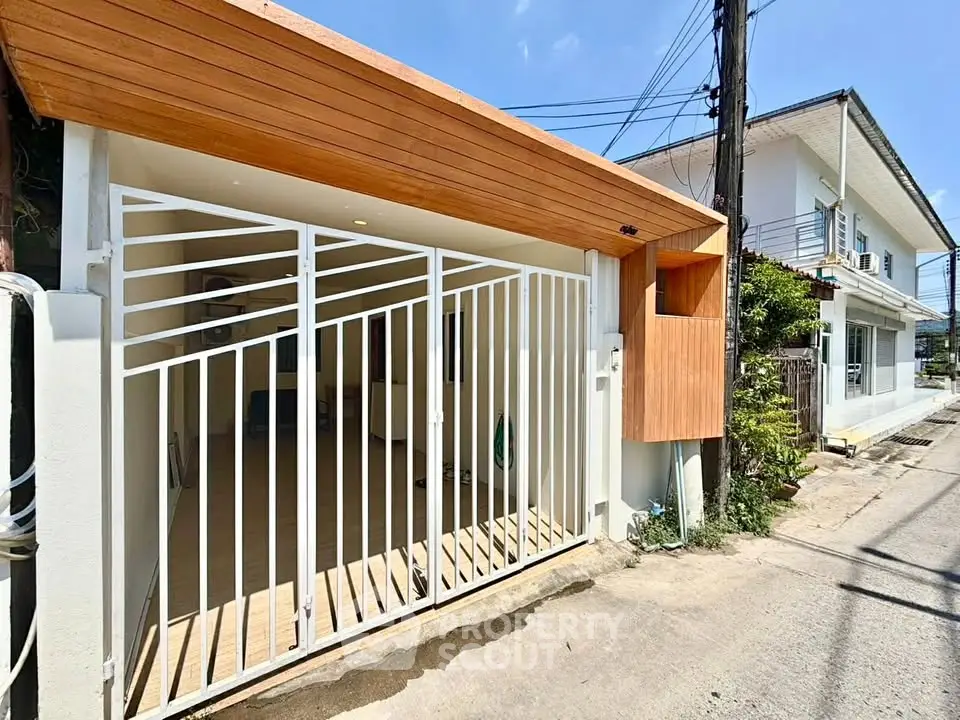 Modern house exterior with wooden accents and gated entrance on a sunny day.