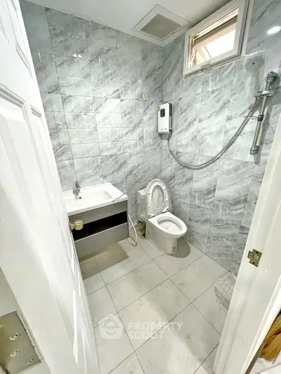 Modern bathroom with marble tiles and compact design, featuring a shower and toilet.