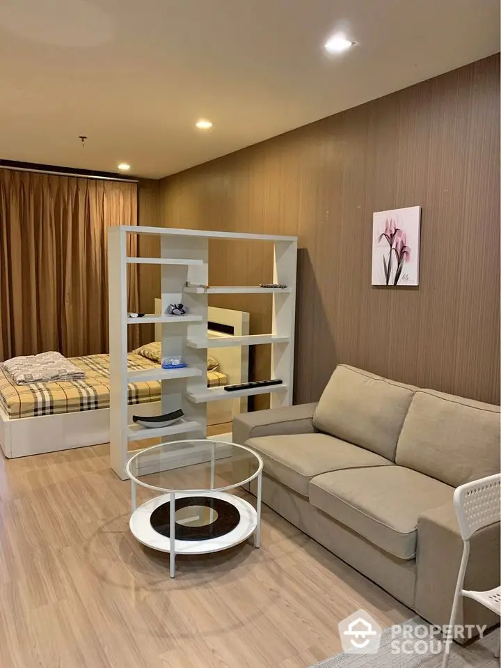 Modern studio apartment with an open layout featuring a cozy living area and a comfortable bedroom space, separated by a stylish shelving unit.