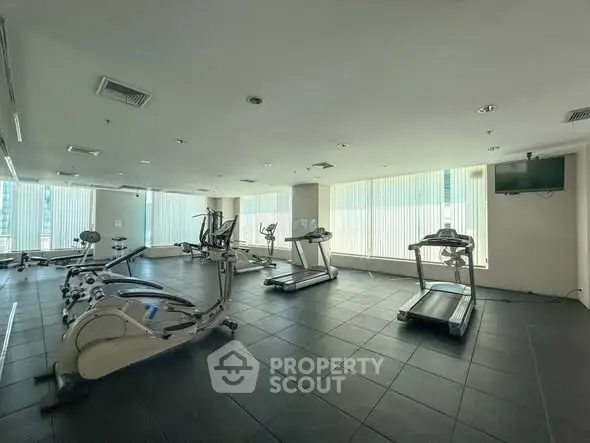Spacious gym with modern equipment and large windows in a real estate property.