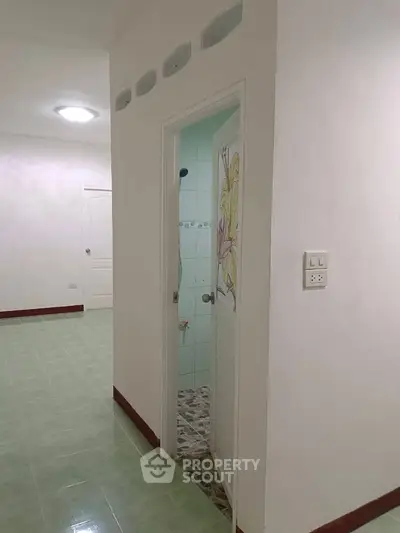 Simple interior hallway with bathroom entrance and green tiled floor.