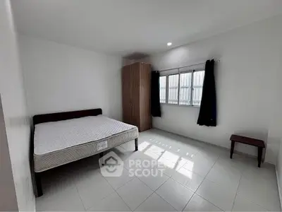 Spacious minimalist bedroom with natural light and simple furnishings.