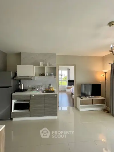 Modern open-layout kitchen with sleek appliances and cozy living area, leading to a bright bedroom.