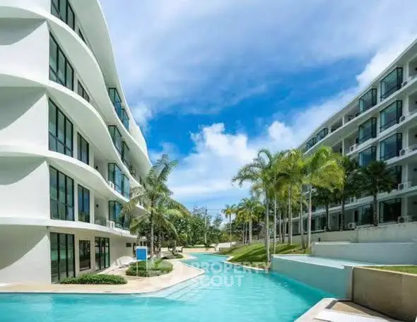 Luxurious modern apartment complex with stunning pool and lush palm trees under a clear blue sky.