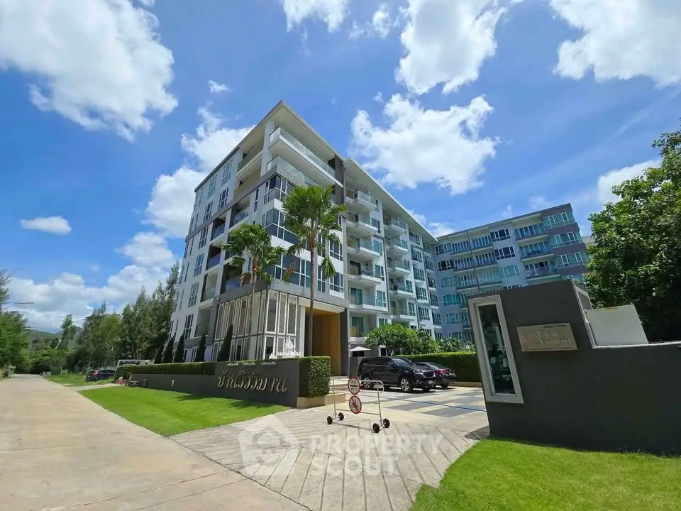 Modern condominium building with lush landscaping and clear blue sky.