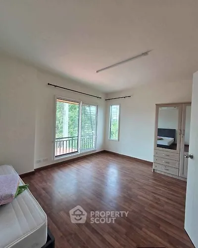 Spacious bedroom with wooden flooring and large windows offering natural light and greenery views.