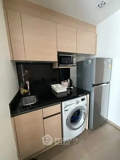 Compact modern kitchen with washing machine and fridge in sleek apartment.