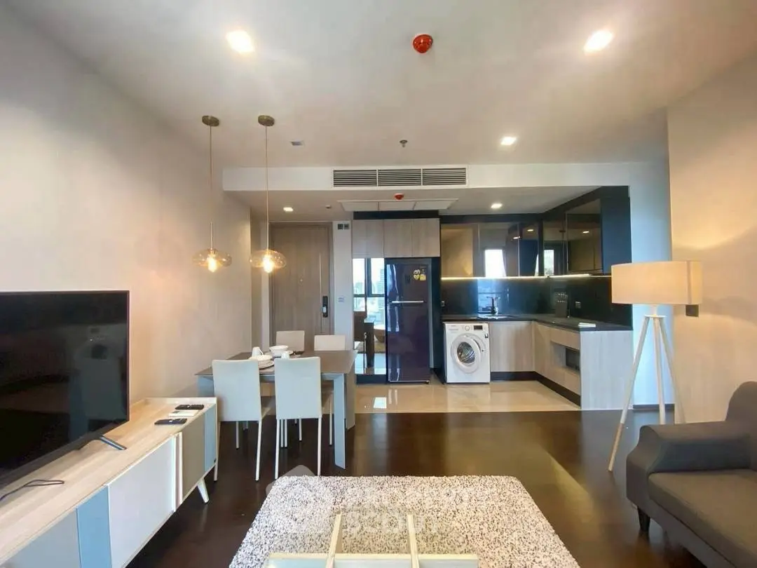 Modern open-plan living room with kitchen and dining area, featuring sleek furniture and appliances.