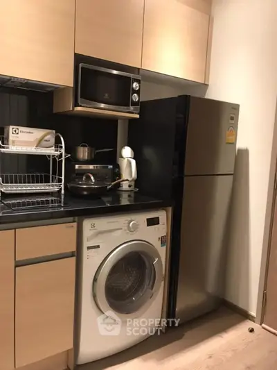 Modern kitchen with washing machine, fridge, and microwave in compact layout.