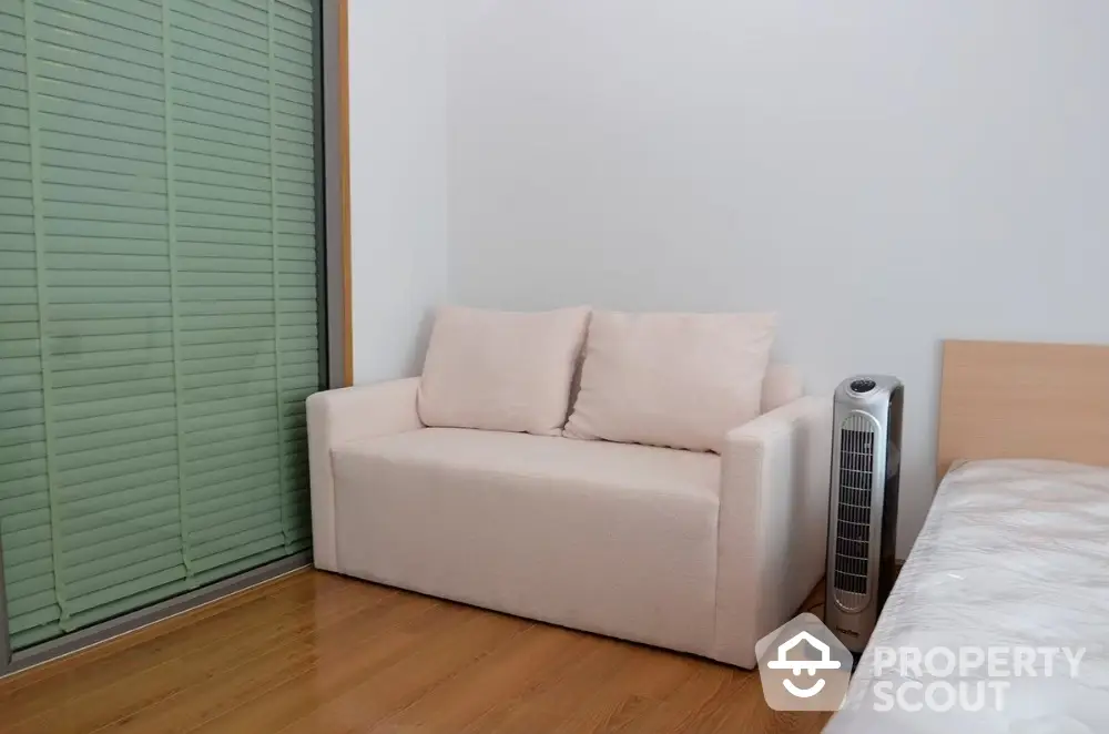 Cozy bedroom with modern sofa and sleek fan, perfect for relaxation.