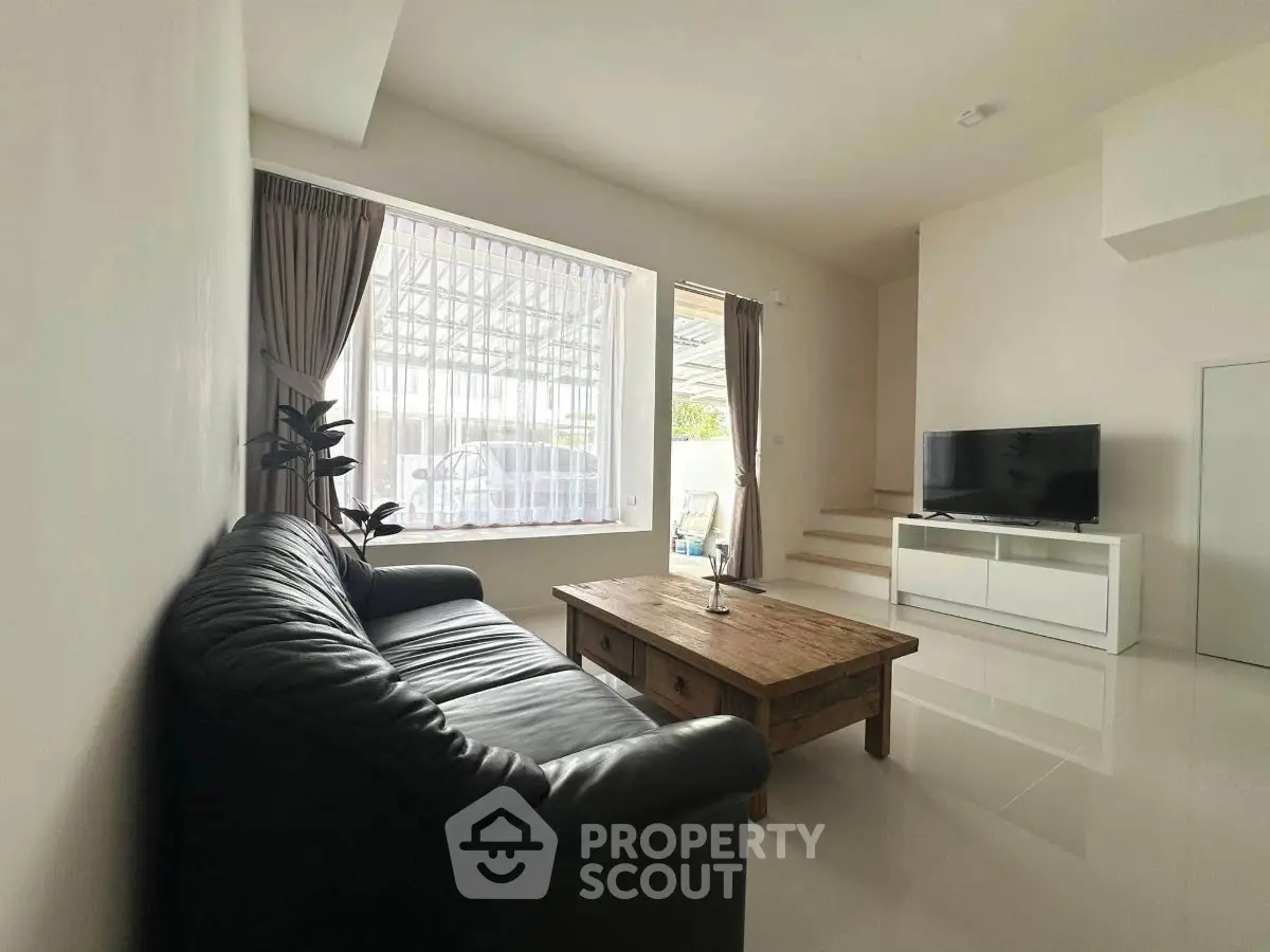 Spacious living room with sleek leather sofa and modern TV setup, perfect for relaxation and entertainment.