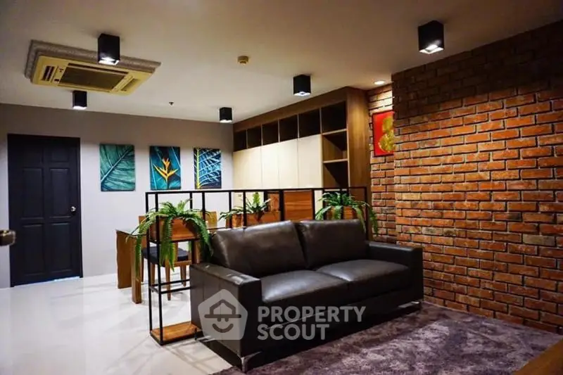 Stylish living room with modern decor, leather sofa, and brick accent wall in a contemporary apartment.