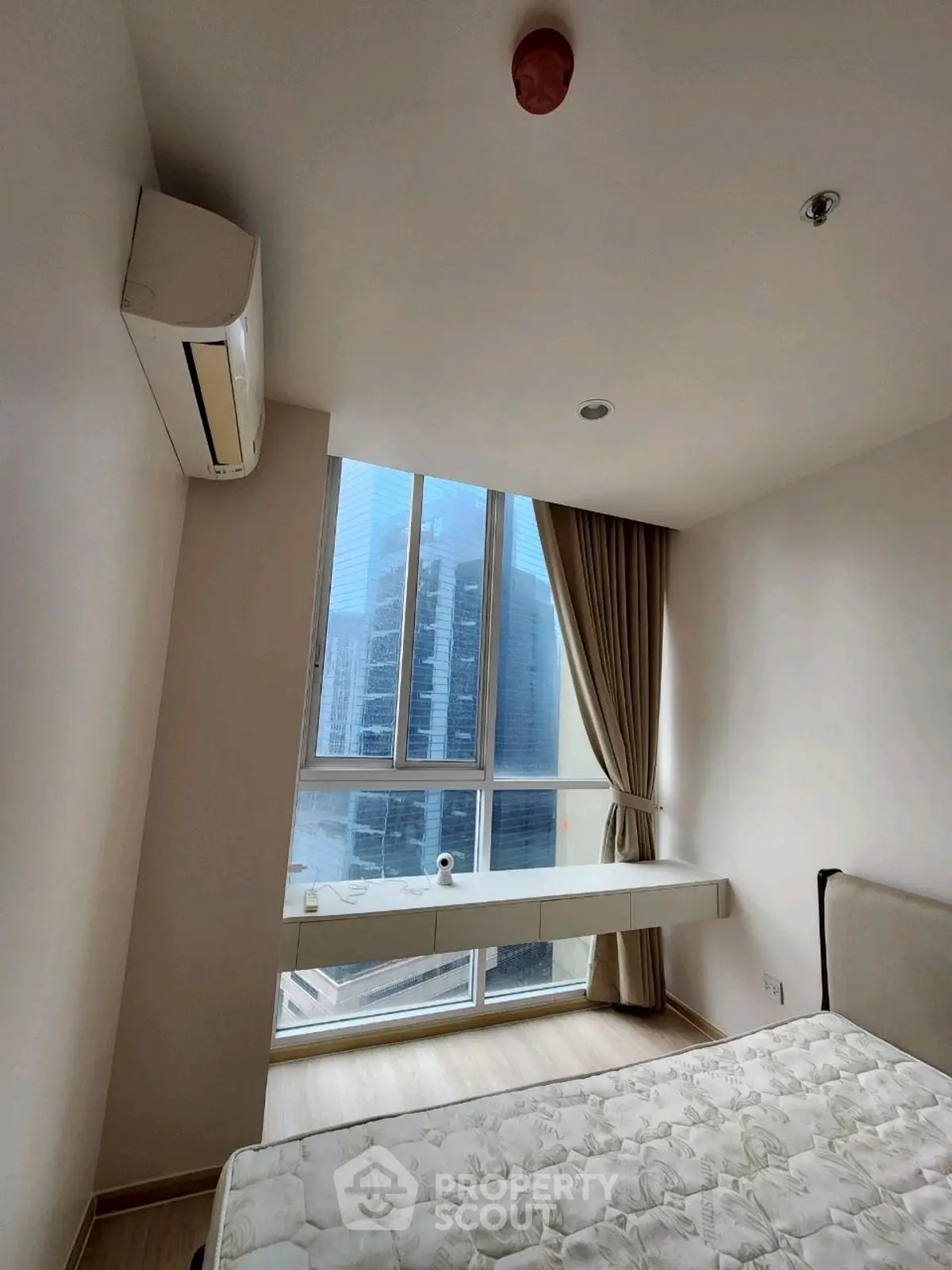 Modern bedroom with large window and city view, featuring air conditioning and minimalist decor.