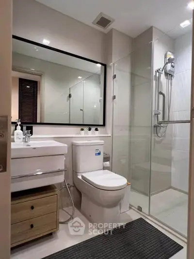 Modern bathroom with glass shower, sleek vanity, and large mirror in a contemporary apartment.