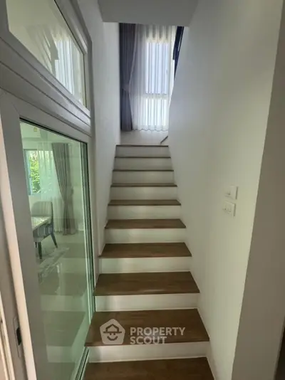 Modern staircase with wooden steps and glass door in bright interior
