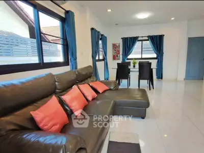 Spacious living room with modern leather sofa and dining area, featuring large windows and elegant decor.