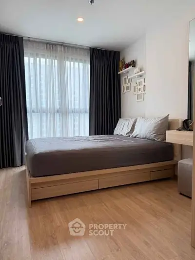 Modern bedroom with wooden flooring and large window, featuring a cozy bed and stylish decor.