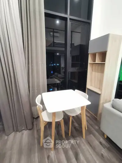 Modern living room with high ceilings and city view, featuring a stylish dining table and chairs.