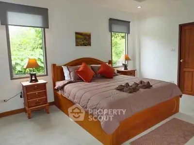 Cozy bedroom with wooden furniture and lush green view from windows.