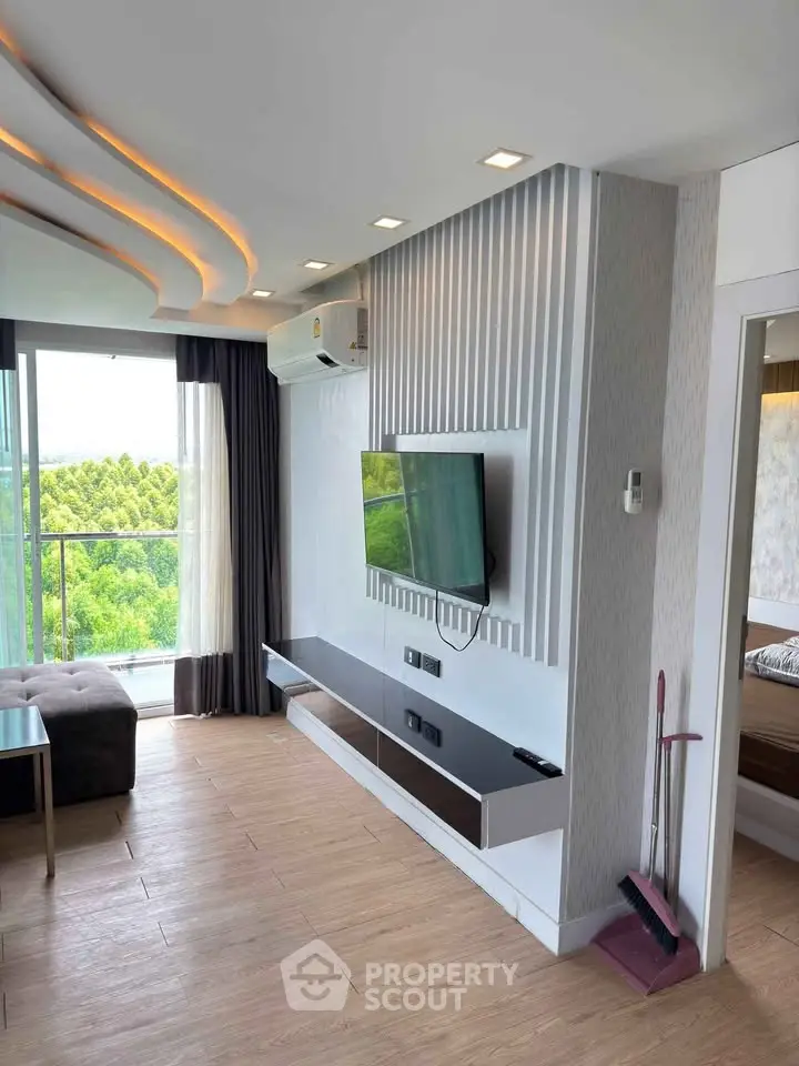 Modern living room with sleek TV setup and large windows offering lush green views.