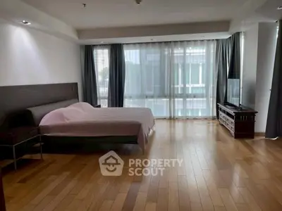Spacious bedroom with large windows and wooden flooring in modern apartment.