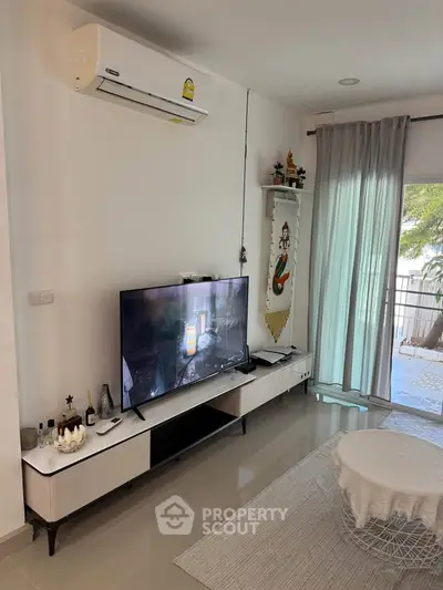 Modern living room with sleek TV setup and balcony view, featuring air conditioning and stylish decor.