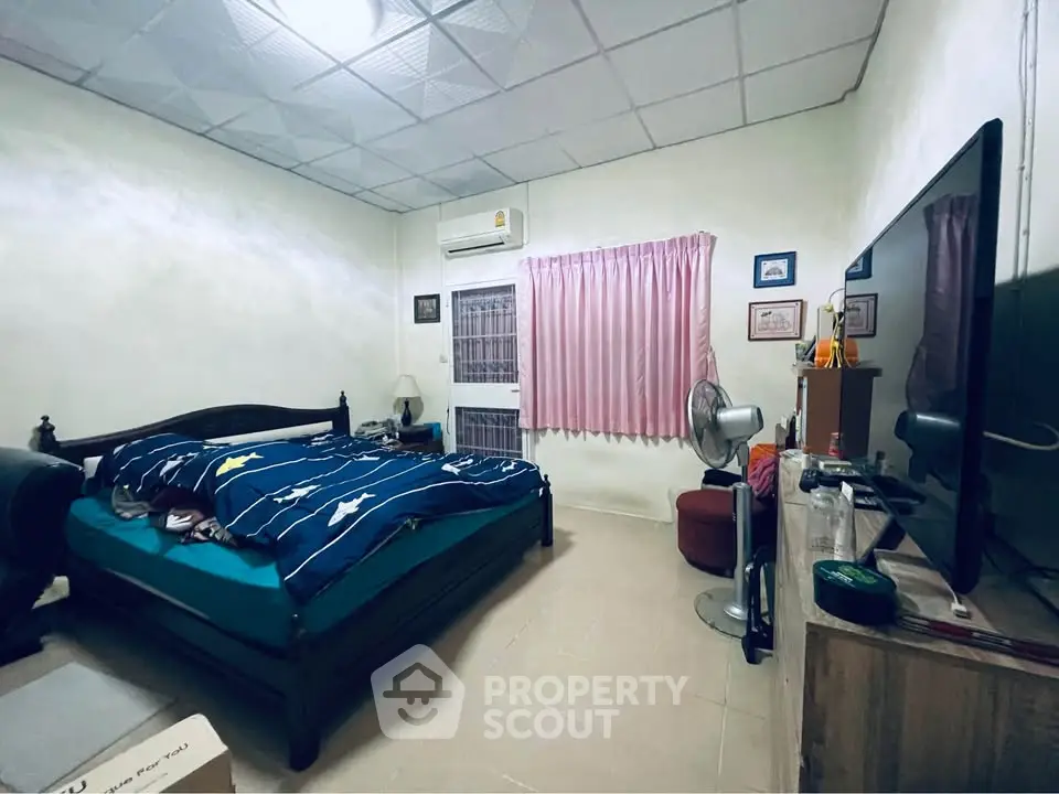 Cozy bedroom with air conditioning and large TV, featuring a comfortable bed and simple decor.