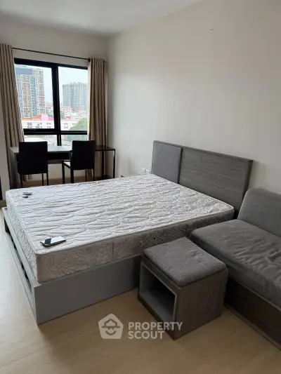 Modern bedroom with large window and city view, featuring a stylish bed and cozy seating area.