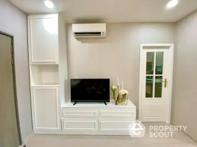 Modern minimalist living room with sleek white entertainment unit, wall-mounted air conditioner, and elegant French doors leading to another room.