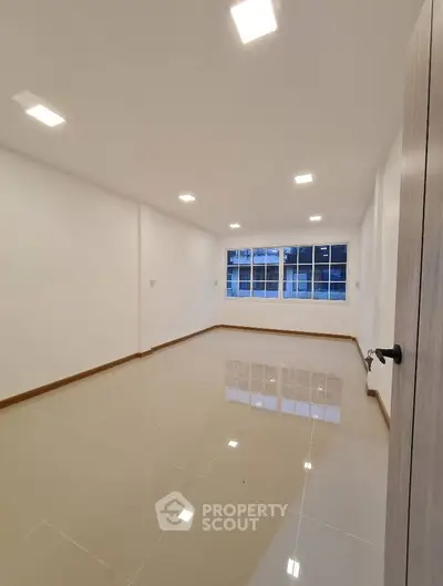 Spacious empty room with glossy tiled flooring and large window, ideal for customization.