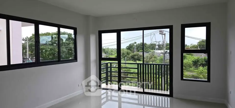 Spacious living room with large windows offering a serene green view, perfect for relaxation.