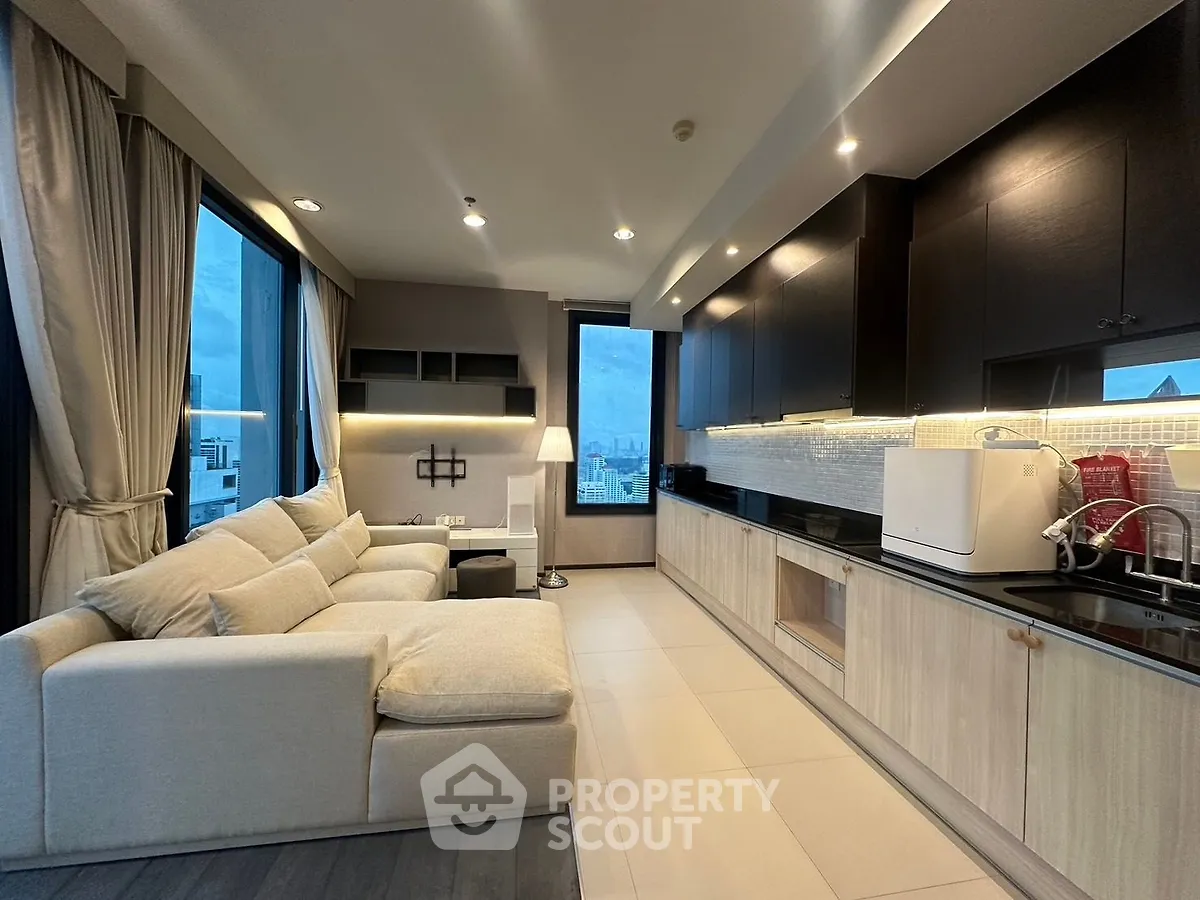 Modern open-layout living room with sleek kitchen and city view, featuring cozy sofa and elegant lighting.