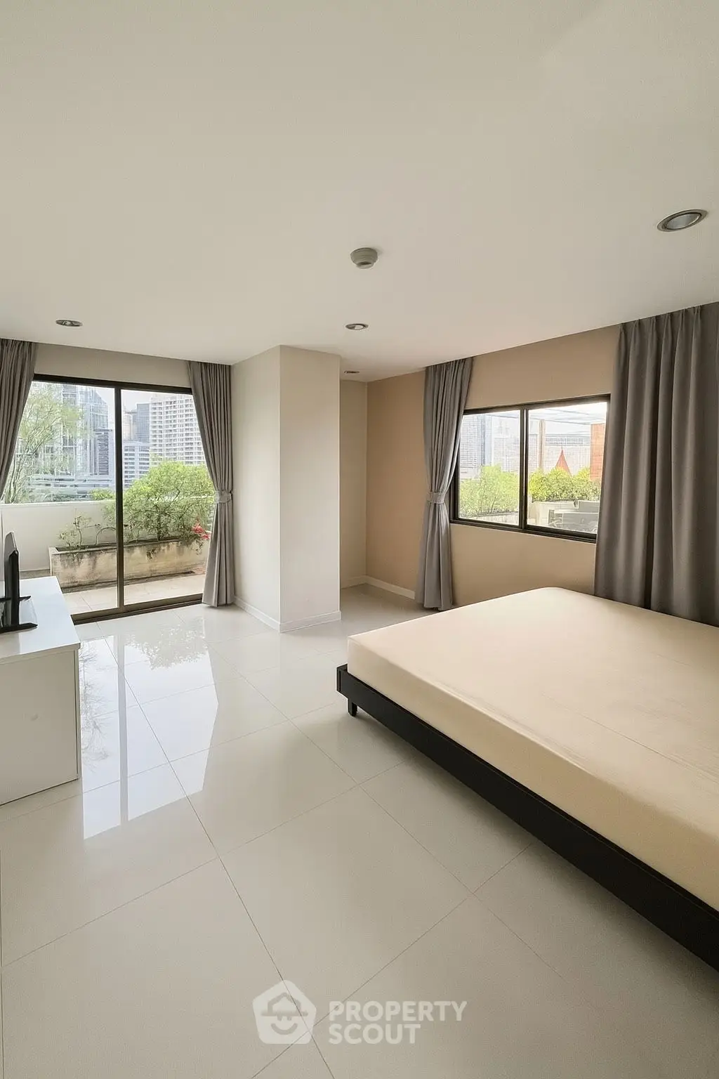 Spacious bedroom with large windows and city view, featuring modern minimalist design and natural light.