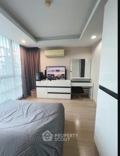 Modern bedroom with sleek furniture and natural light, featuring a cozy workspace and entertainment setup.