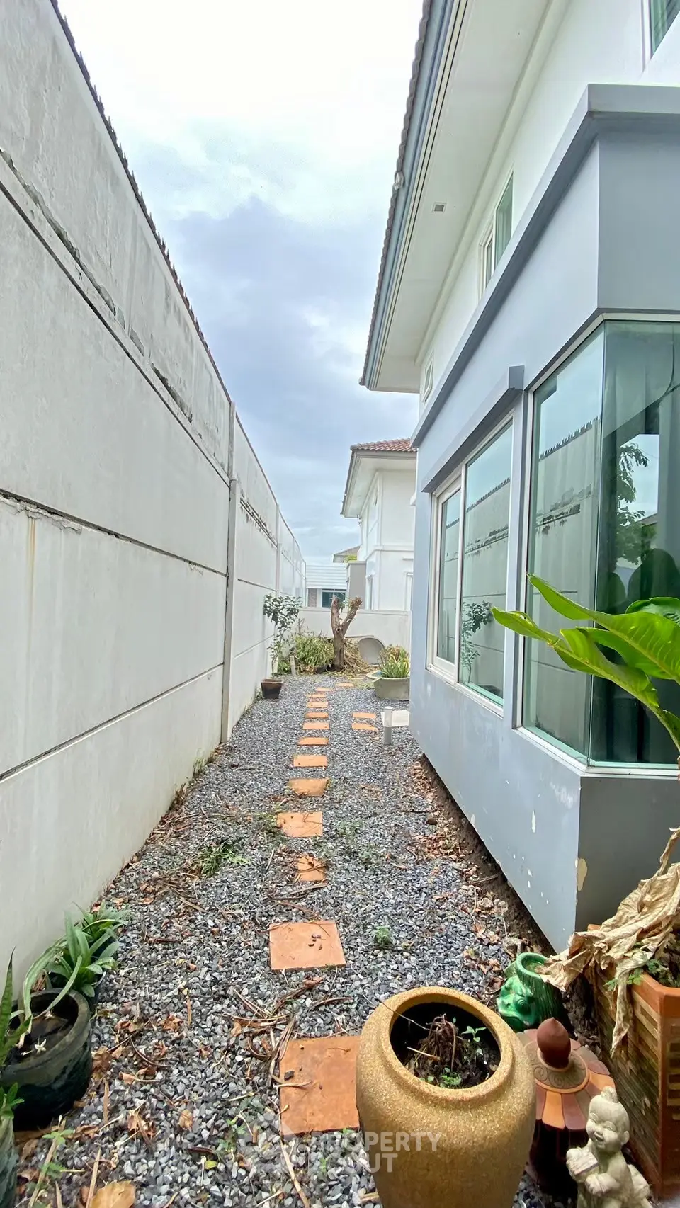 Charming side pathway with gravel and potted plants beside modern house exterior.